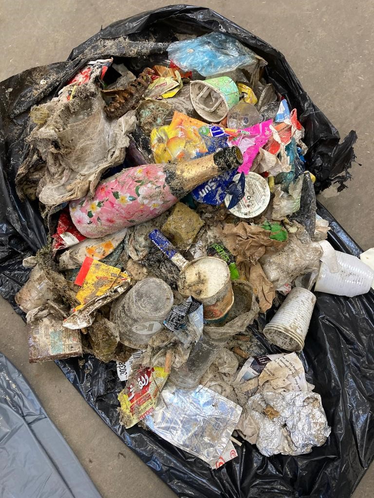 Bilden visar skräp som har plockats vid badstranden, ett par skor och olika plastföremål