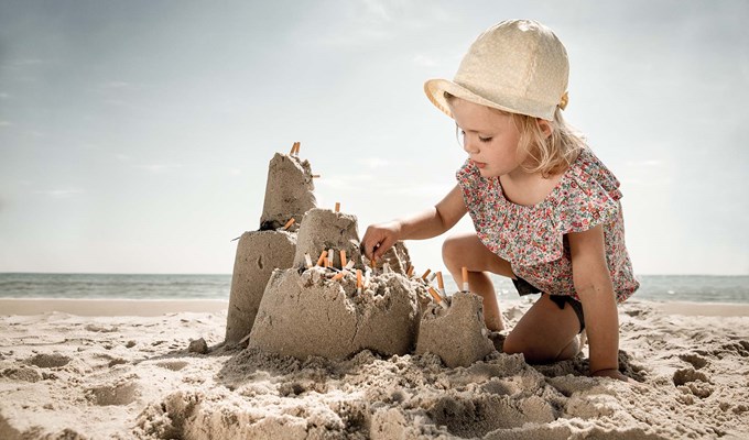 Skylt som visar en flicka som dekorerar ett sandslott med fimpar