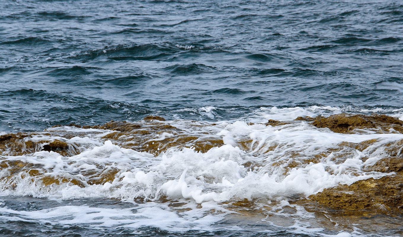 Inzoomat på vågor som slår mot en brun klippa
