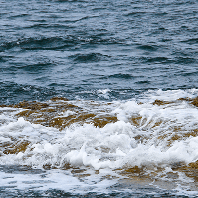 Inzoomat på vågor som slår mot en brun klippa
